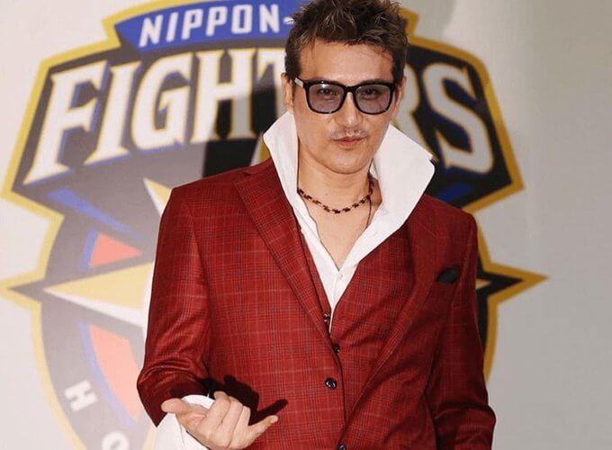 新庄剛志がサングラスをしてワインレッドのスーツを着ている就任会見の画像